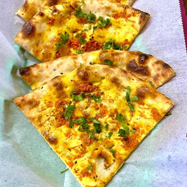 Four pieces of golden-brown Indian naan bread, topped with yellow spices and fresh green cilantro.