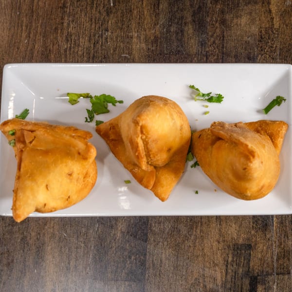 Three golden-brown Indian samosas garnished with cilantro on a white rectangular plate.