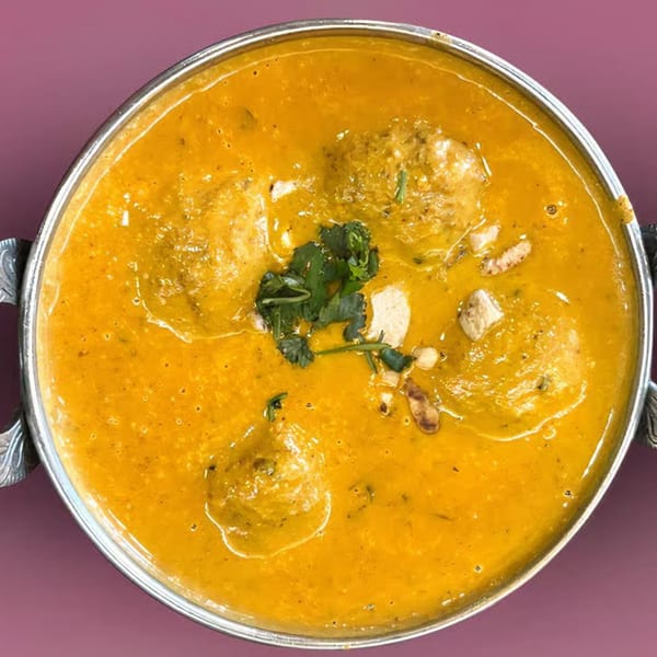 Overhead view of a metal bowl filled with a rich orange Indian curry, garnished with cilantro.