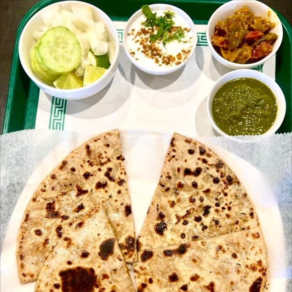 Indian flatbread with sides of cucumber, onion, raita, chutney, and a vegetable dish.