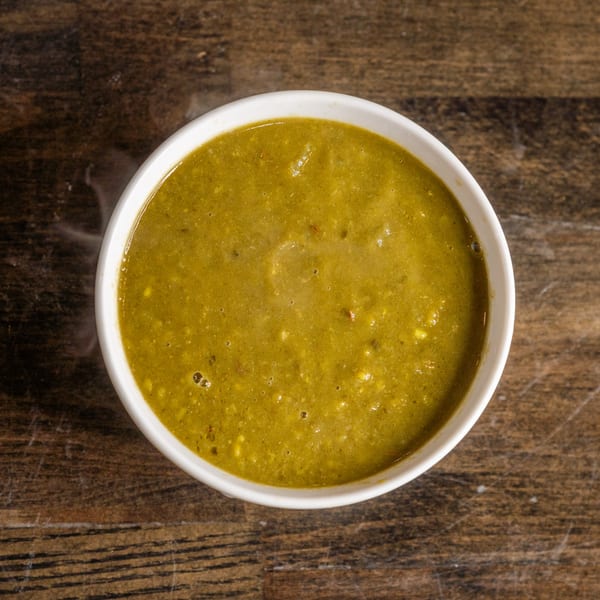Overhead view of a white bowl filled with steaming, thick green Indian curry on a wooden table.