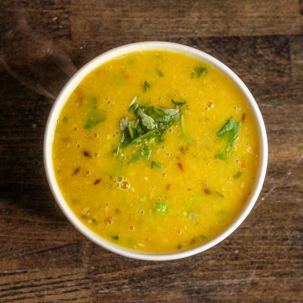 Overhead view of a white bowl filled with yellow Indian dal, garnished with fresh green cilantro.