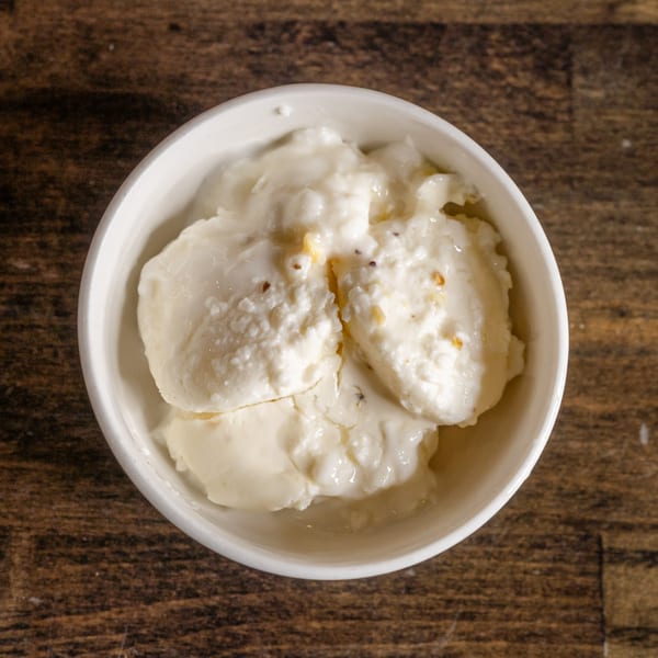 Top-down view of a white bowl filled with creamy, white Indian dessert on a wooden table.